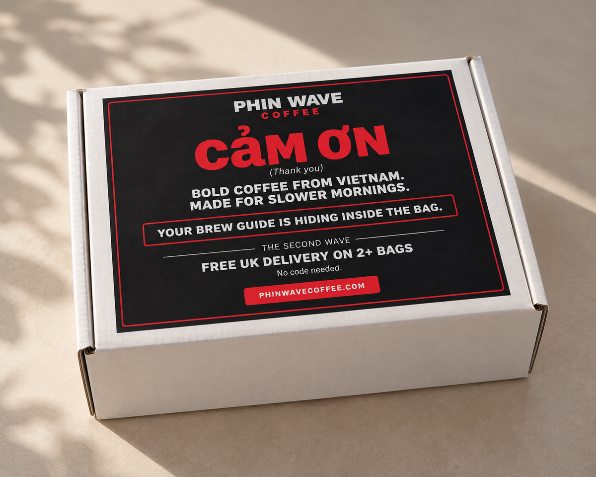 A white cardboard box for PHIN WAVE COFFEE with a large black label featuring bold red and white text, photographed on a light beige surface with soft shadows.